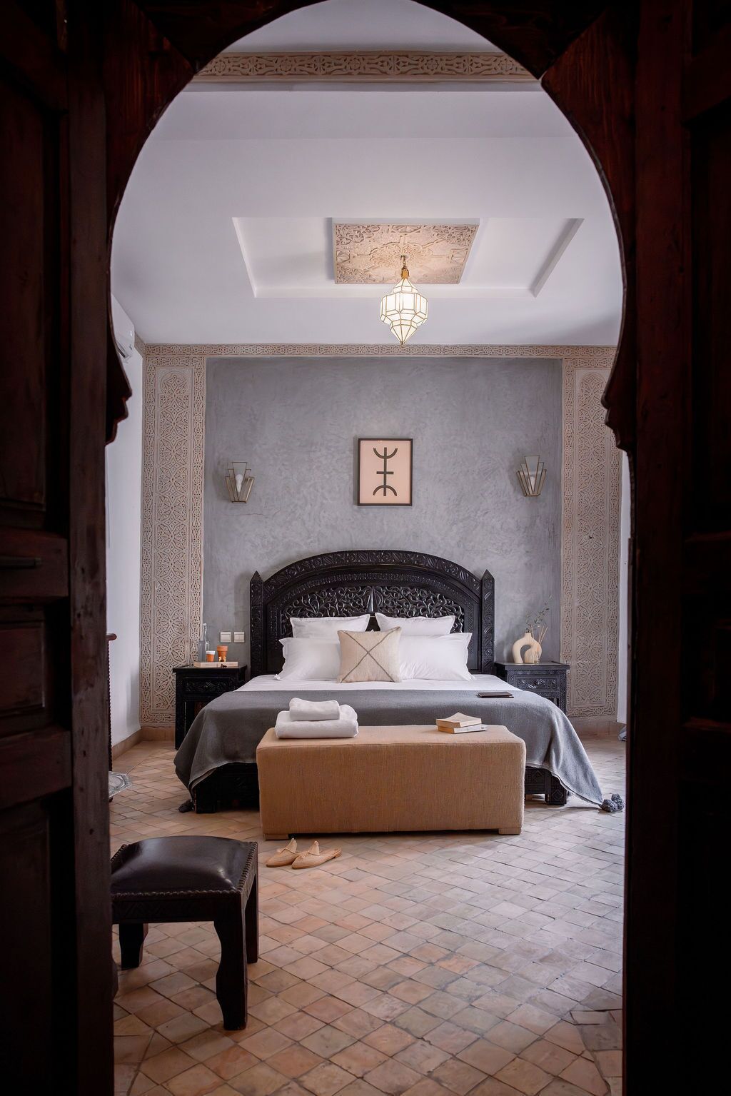 A bedroom with a large bed, a bench, a nightstand, and a wall-mounted light fixture.