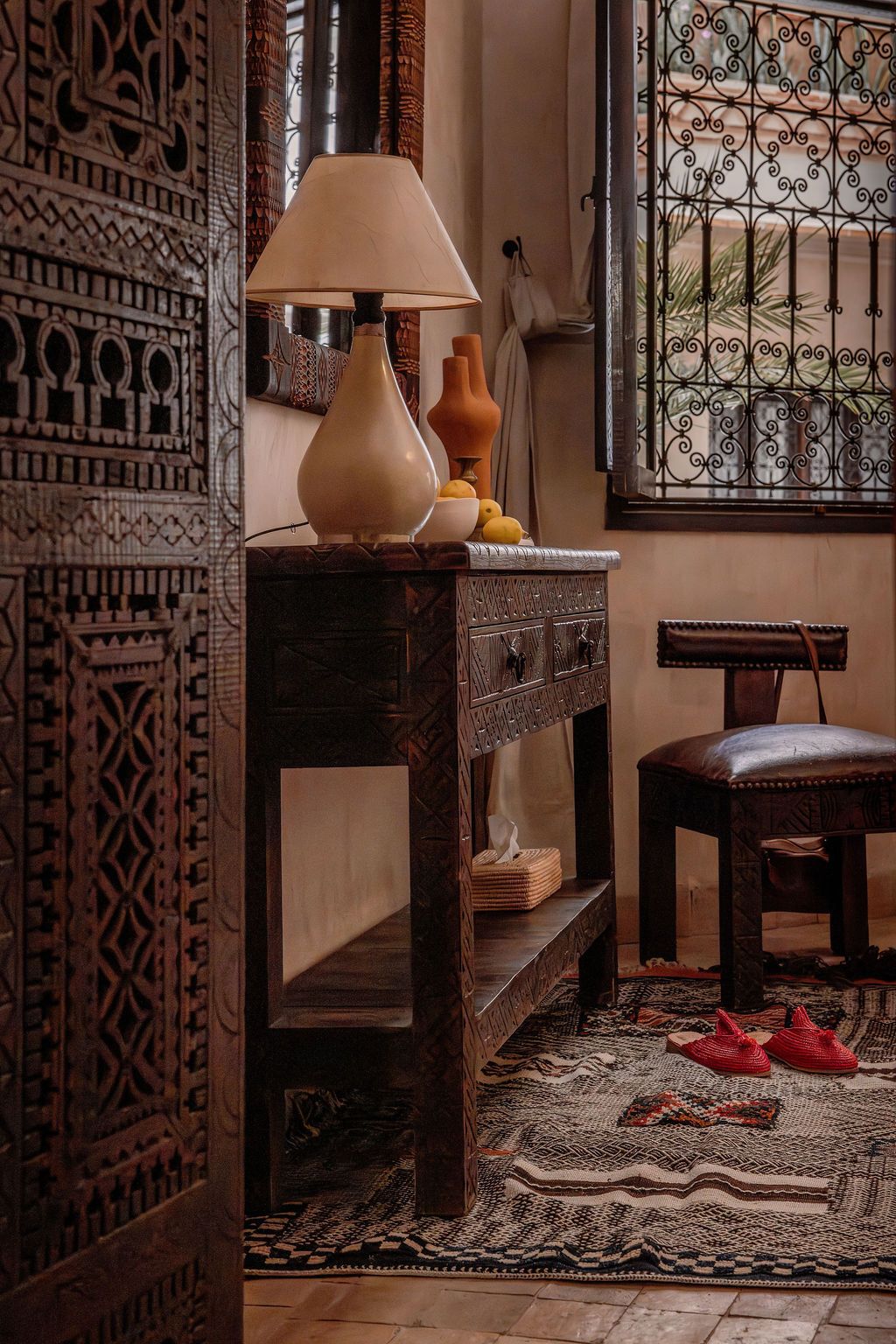 A room with a wooden cabinet, a lamp, a chair, and a patterned rug.
