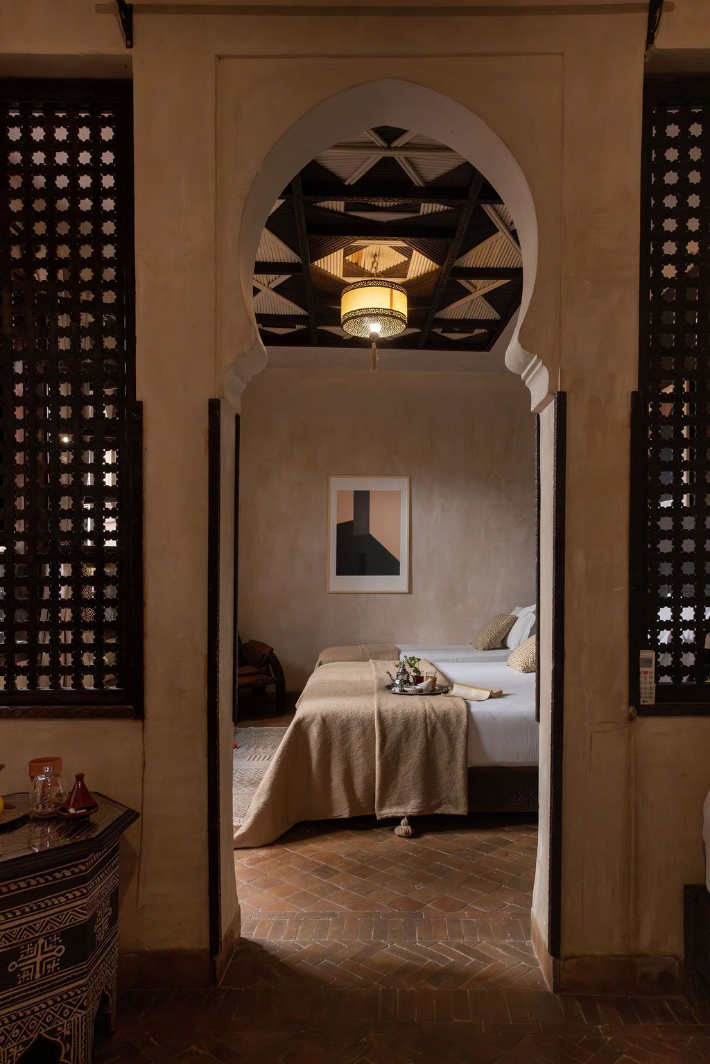 A hotel room with a bed, a nightstand, a decorative wall piece, and a patterned floor.