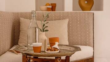 Un coin salon accueillant avec un canapé à motifs, une petite table en bois sur laquelle se trouvent une carafe en verre, une tasse et une assiette de biscuits.
