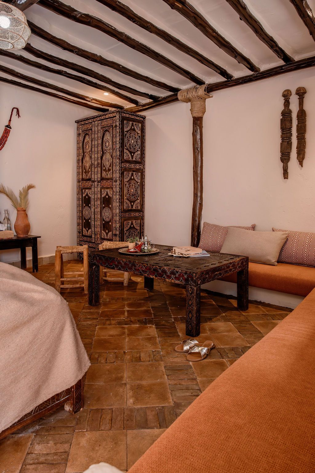 Una habitación con un mueble de madera con motivos, una mesa de madera, un sofá y un suelo de baldosas.