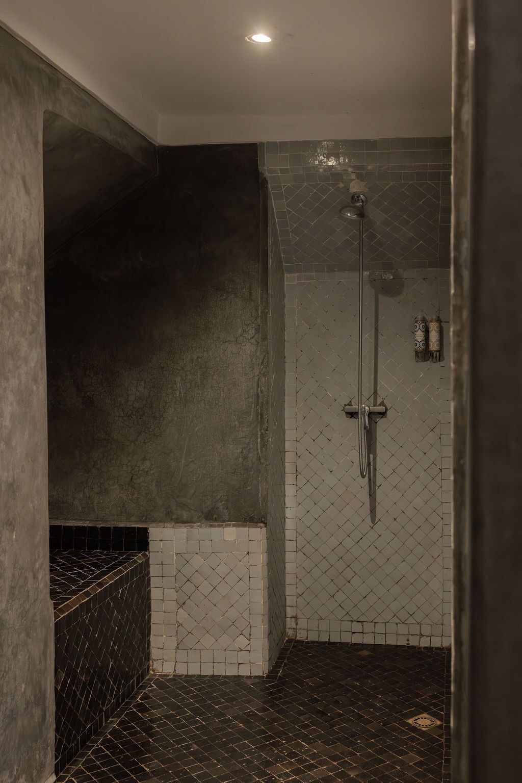 A shower area with a tiled wall and floor, a handheld showerhead, and a visible drain.