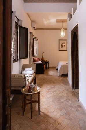 A hallway with a sofa, a small table with drinks, and a bed in the distance. - Les Sources Berbères Riad & Spa (Marrakech)