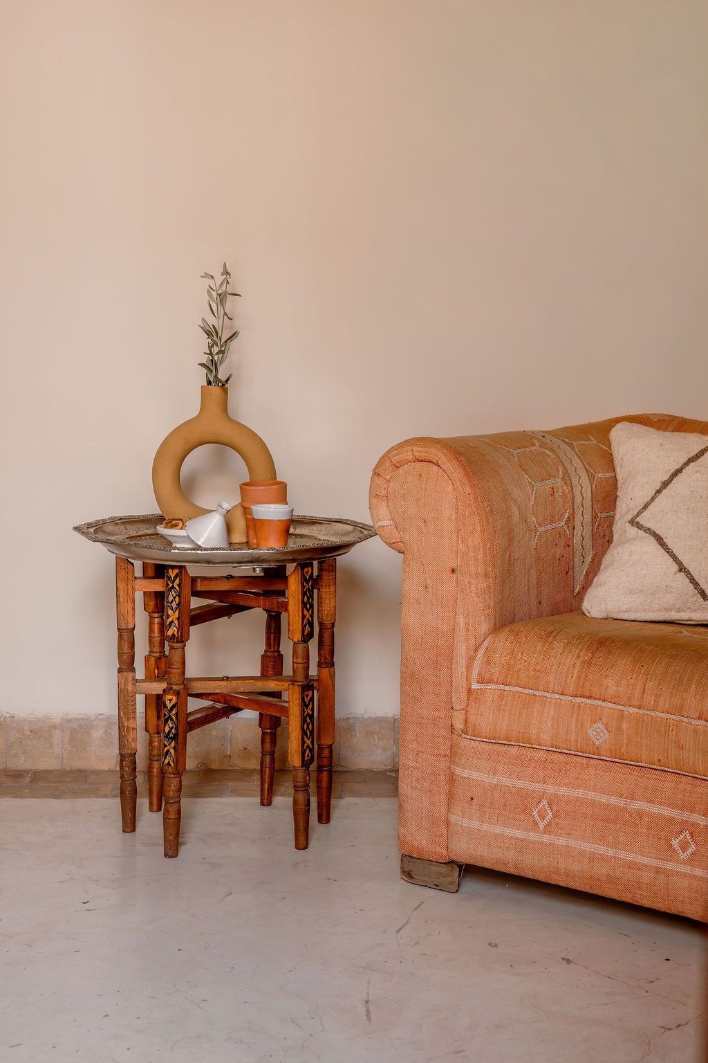 Une table en bois avec un vase et une tasse, un canapé à motifs et un mur uni.