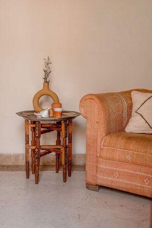 Uma mesa de madeira com um vaso e uma xícara, um sofá estampado e uma parede lisa.