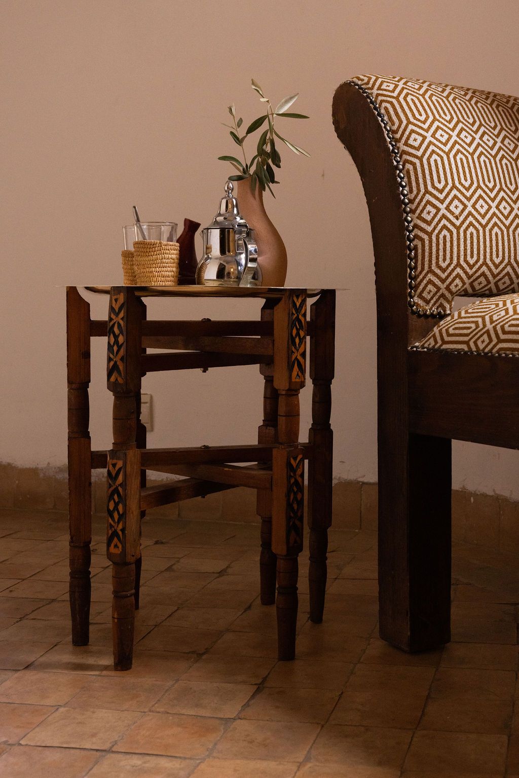 A wooden table with a woven basket and a metal pitcher, placed next to a patterned sofa.