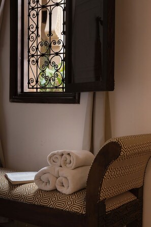Una habitación con ventana que tiene rejas decorativas de hierro, una silla con cojín estampado y una toalla enrollada en el asiento.