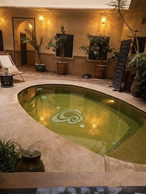 A pool with a geometric design, surrounded by potted plants and a lounge area with a chair and a table. - Les Sources Berbères Riad & Spa (Marrakech)