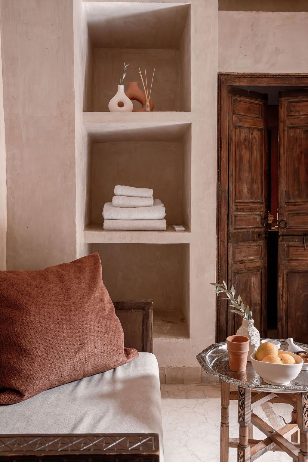 A room with a sofa, a table with a bowl of fruit, and wooden shelves with folded towels.