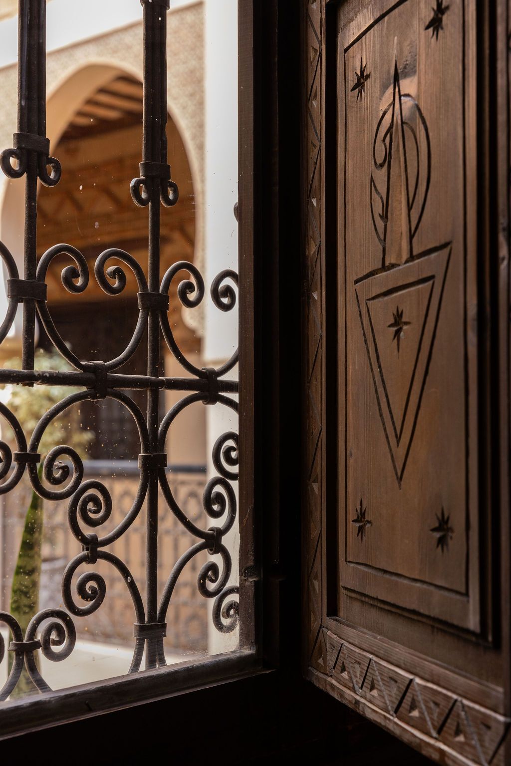 A wrought iron gate with intricate scrollwork, a wooden door with a geometric design, and a view of an archway outside.