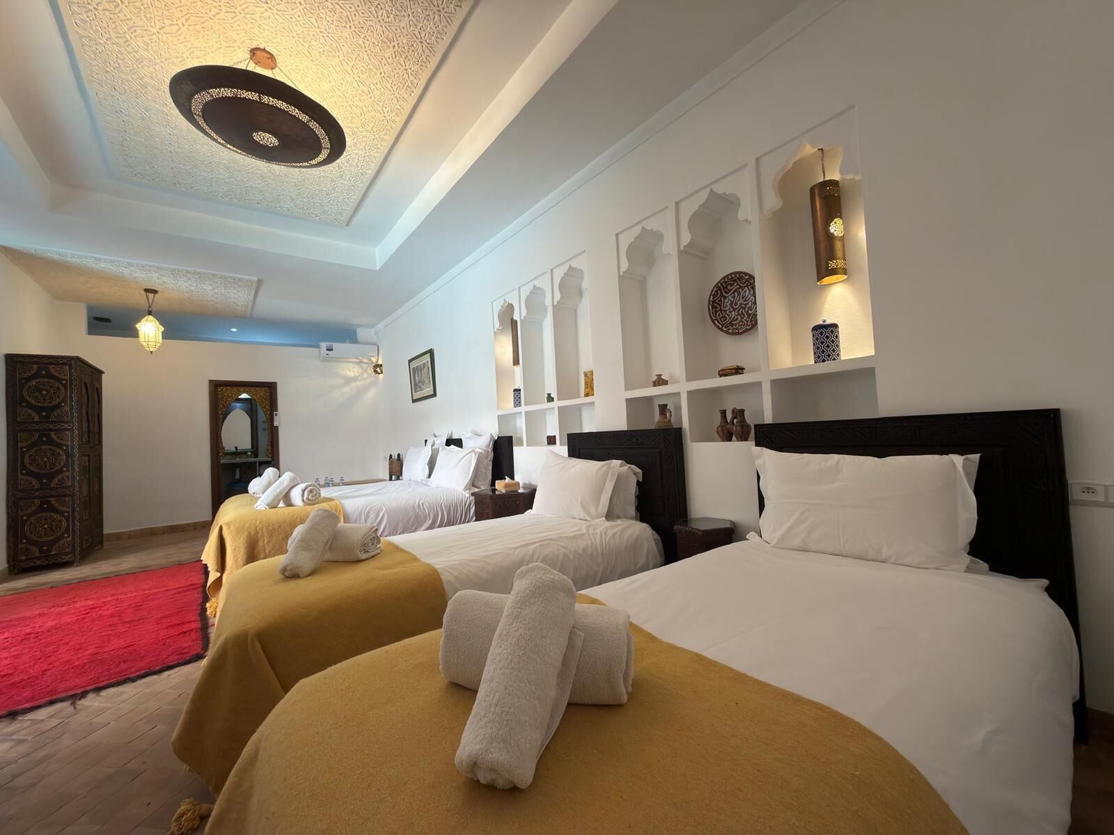 Une chambre d’hôtel avec deux lits, une moquette rouge, un mur décoratif et un luminaire au plafond.