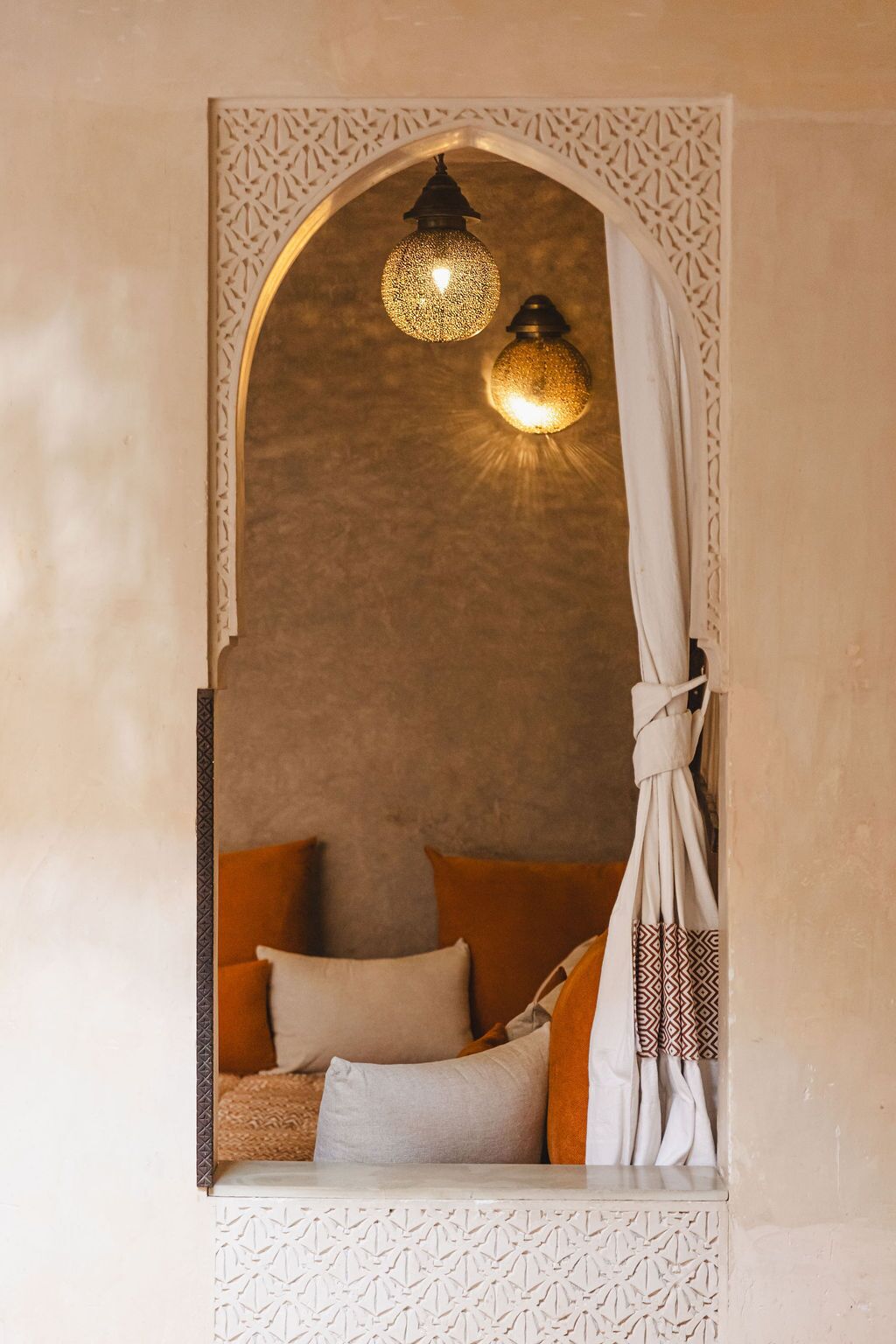 A cozy room with a decorative archway, a hanging light fixture, and a bed with pillows.