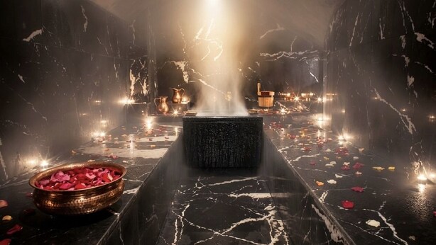 A dimly lit room with a central water feature, a bowl of rose petals, and a marble floor. - Les Sources Berbères Riad & Spa (Marrakech)
