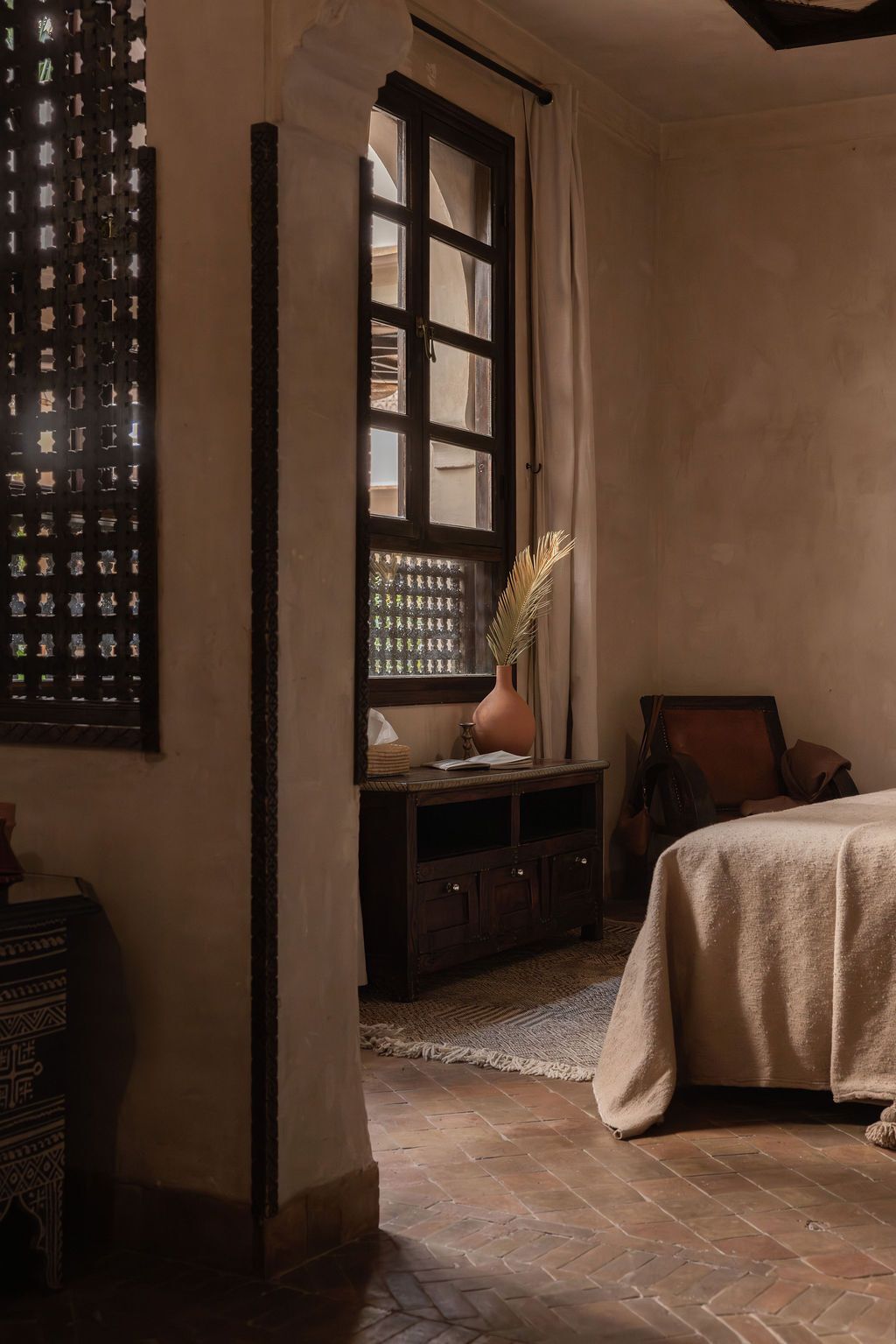 Una habitación con un ventanal grande, una cama, un aparador y un adorno en la pared.