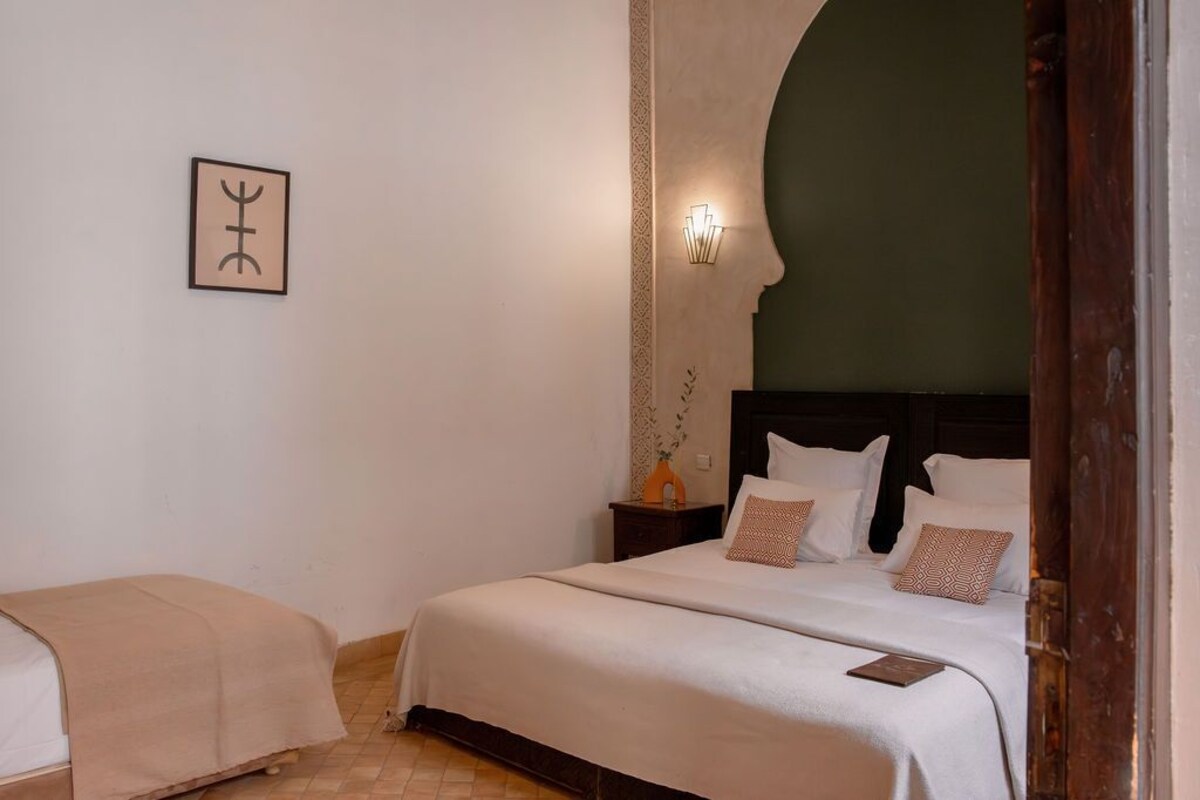 A hotel room with two beds, a nightstand, a wall-mounted light, and a framed picture.