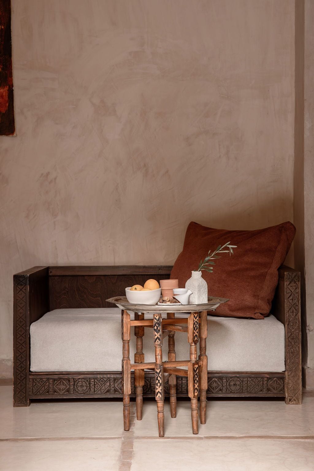 A sofa with a cushion, a small wooden table with a tray, and a vase with a plant.