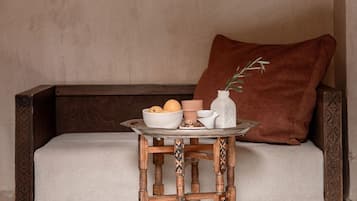 A sofa with a cushion, a small wooden table with a tray, and a vase with a plant.