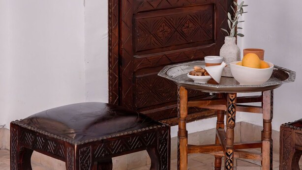 A wooden door with intricate carvings, a round table with a bowl and a vase, and a matching wooden stool. - Les Sources Berbères Riad & Spa (Marrakech)