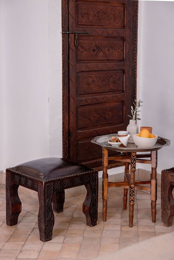A wooden door with intricate carvings, a round table with a bowl and a vase, and a matching wooden stool. - Les Sources Berbères Riad & Spa (Marrakech)