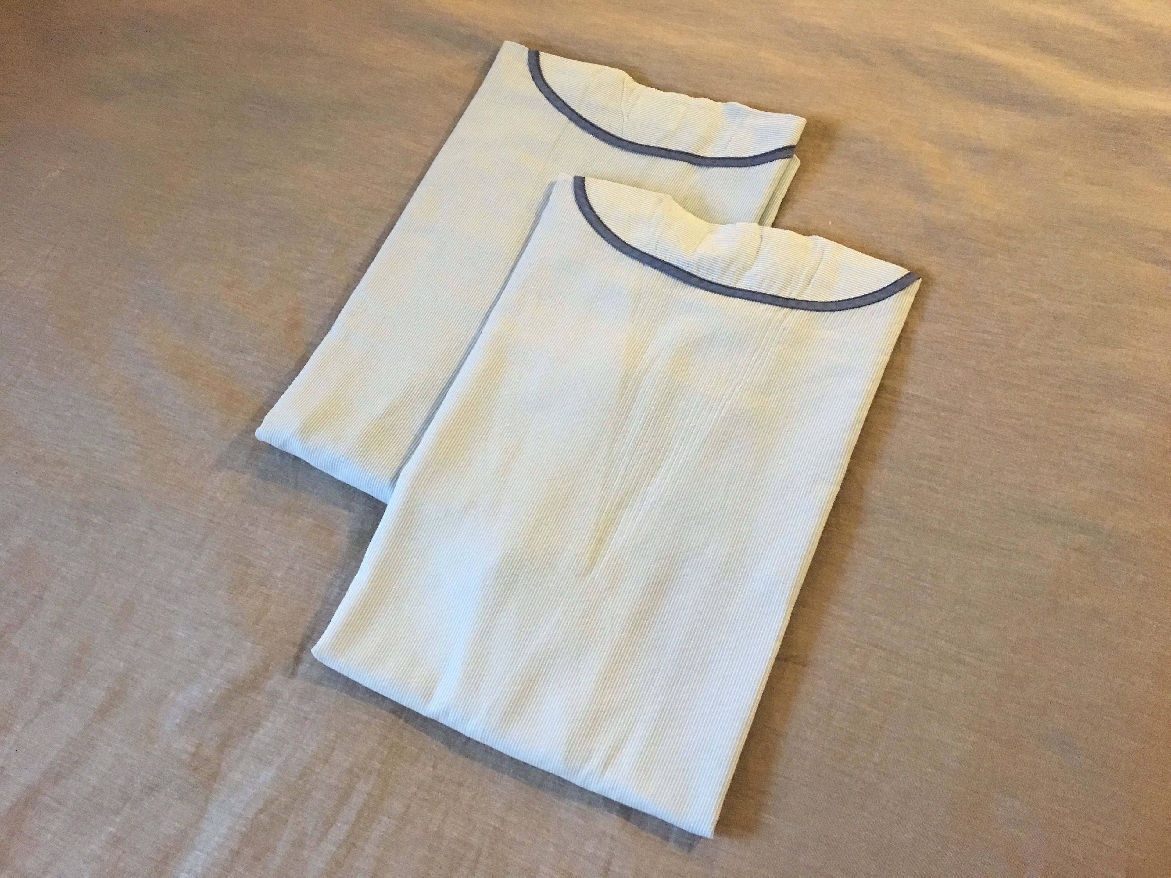 Two white shirts with dark blue trim laid out on a wooden surface.