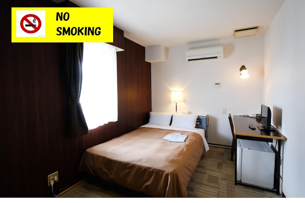 A hotel room with a bed, desk, and a 'NO SMOKING' sign.