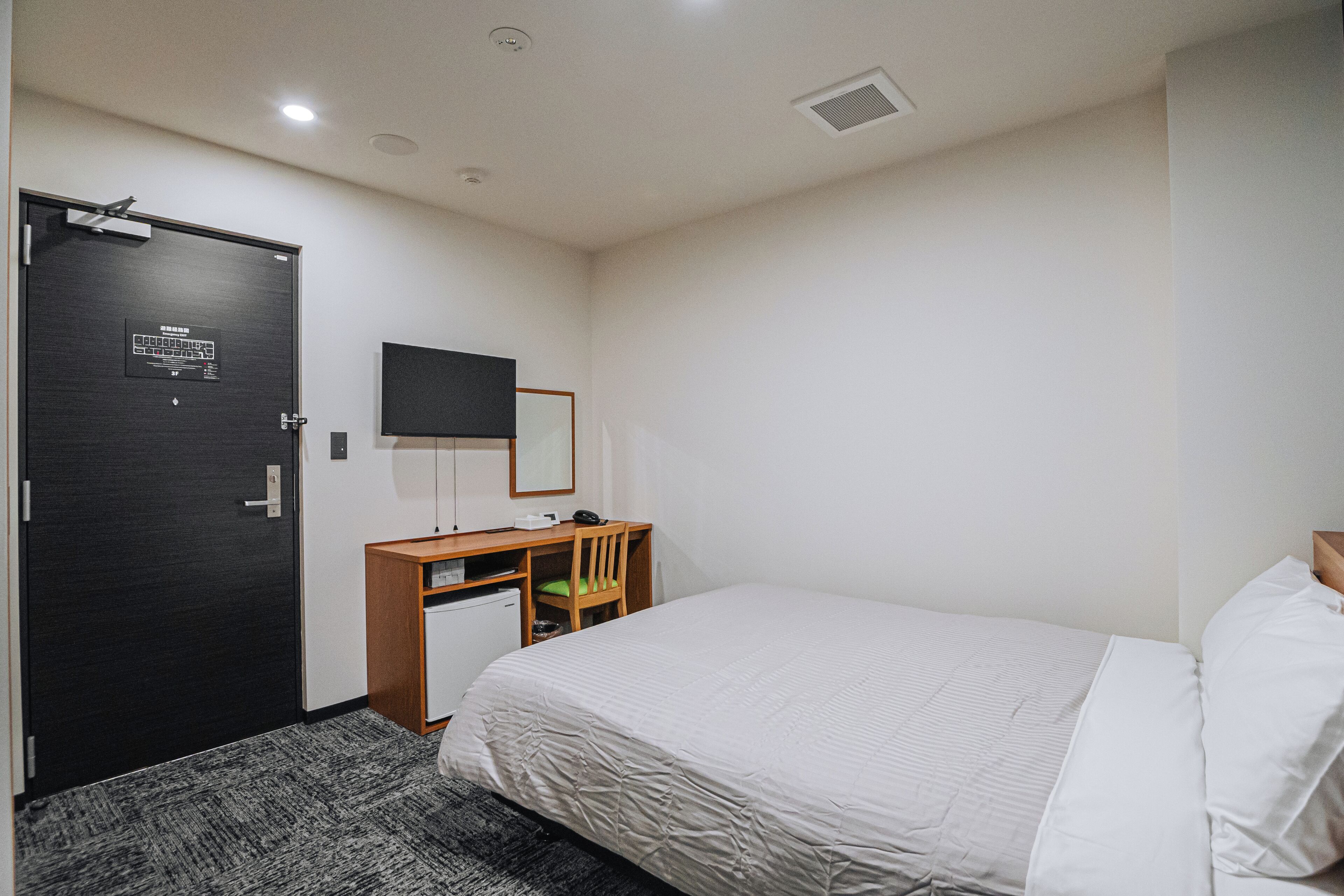A hotel room with a bed, a desk, a chair, a television, and a door.