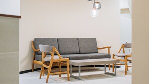 A modern living room with a grey sofa, wooden chairs, a coffee table, and pendant lights. - Business Inn SUNHOTEL (Machida)