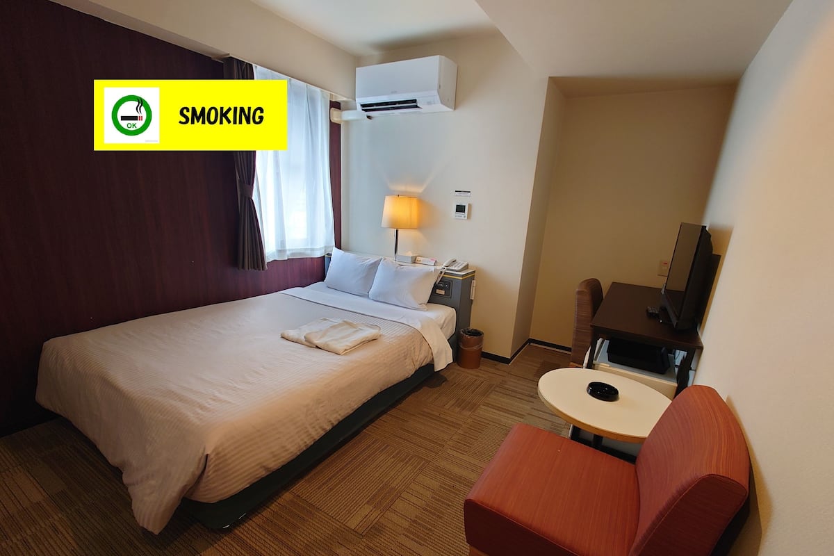 A hotel room with a bed, a desk, a chair, a lamp, and a television.