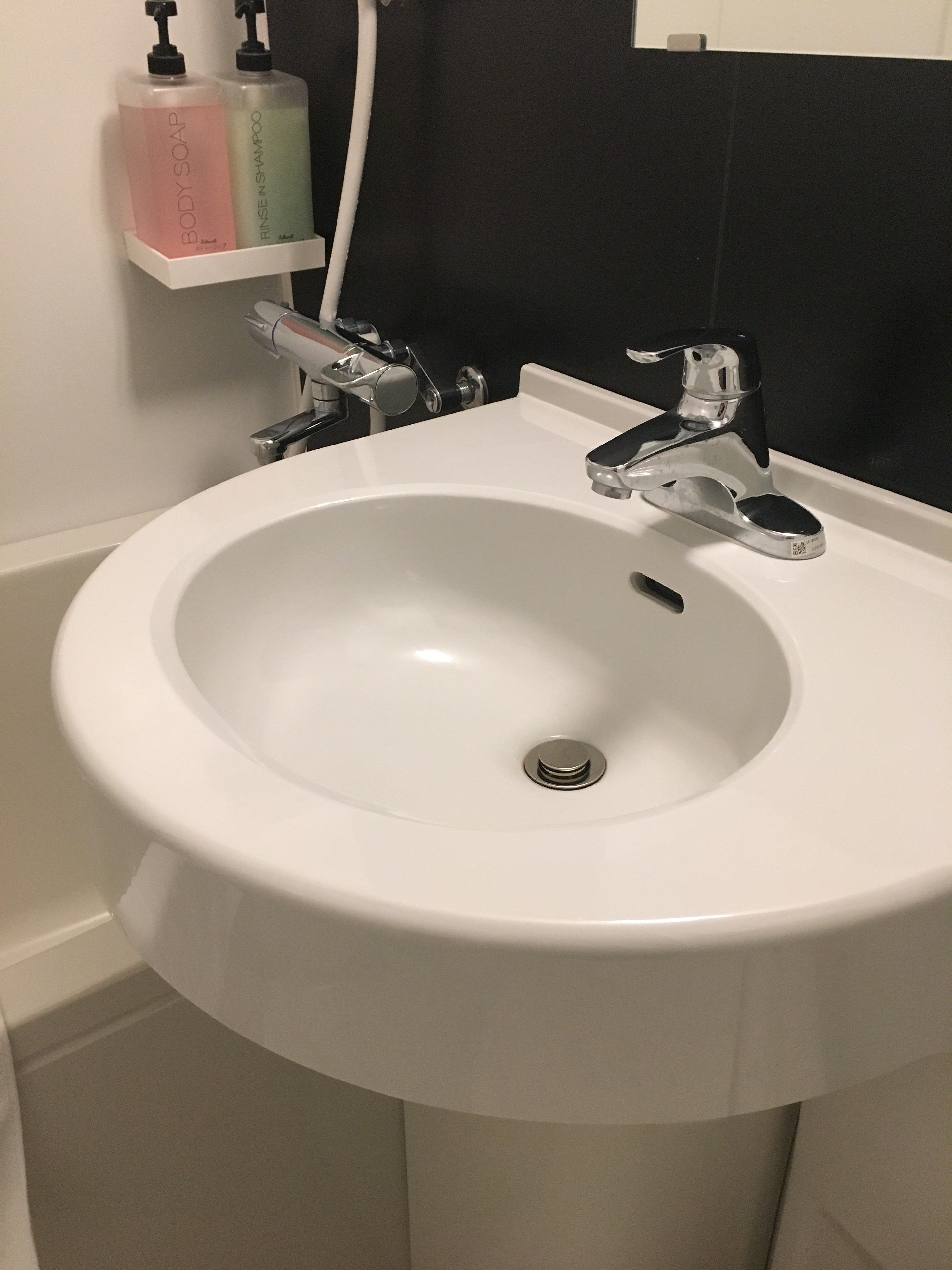 Un lavamanos blanco con grifo cromado, una pared blanca y un salpicadero de azulejos negros.