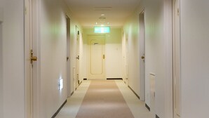 A hotel hallway with doors on both sides, a carpeted floor, and a light green exit sign on the wall. - Business Inn SUNHOTEL (Machida)