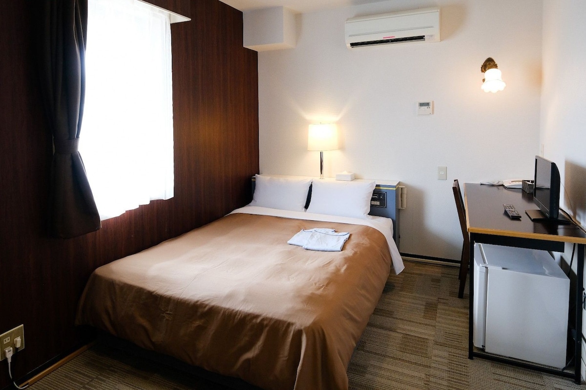 A hotel room with a bed, desk, and a 'NO SMOKING' sign.