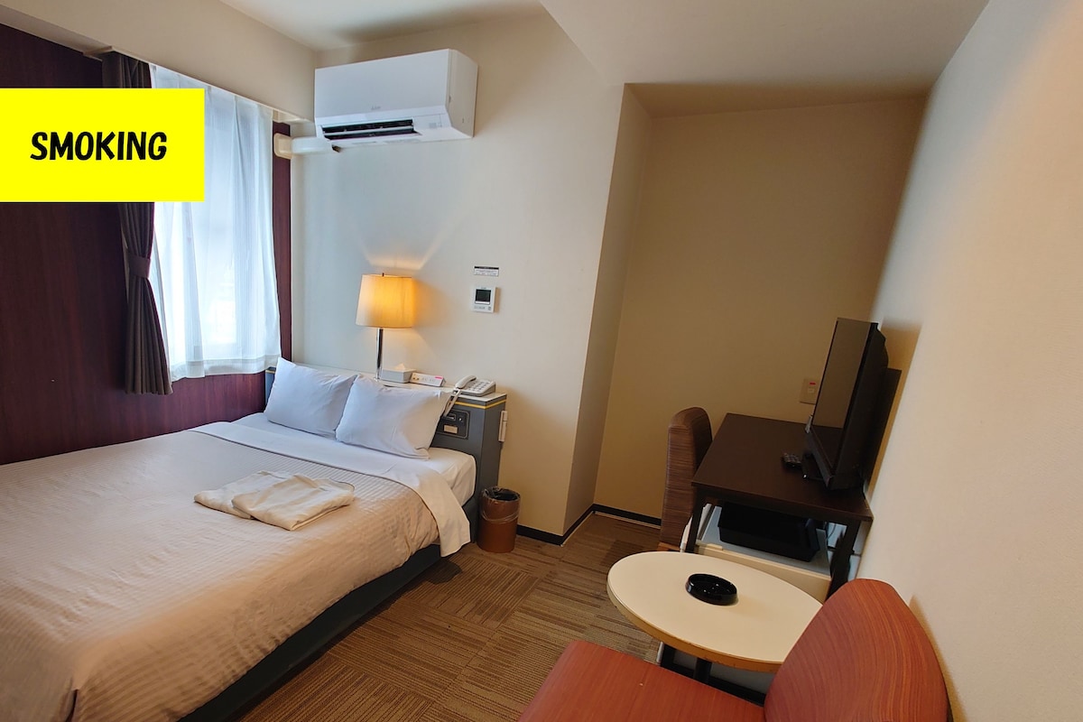 A hotel room with a bed, a desk, a chair, a lamp, and a television.