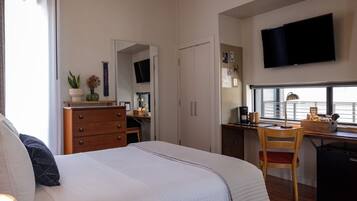 A bedroom with a bed, a desk, a chair, a TV, and a window.