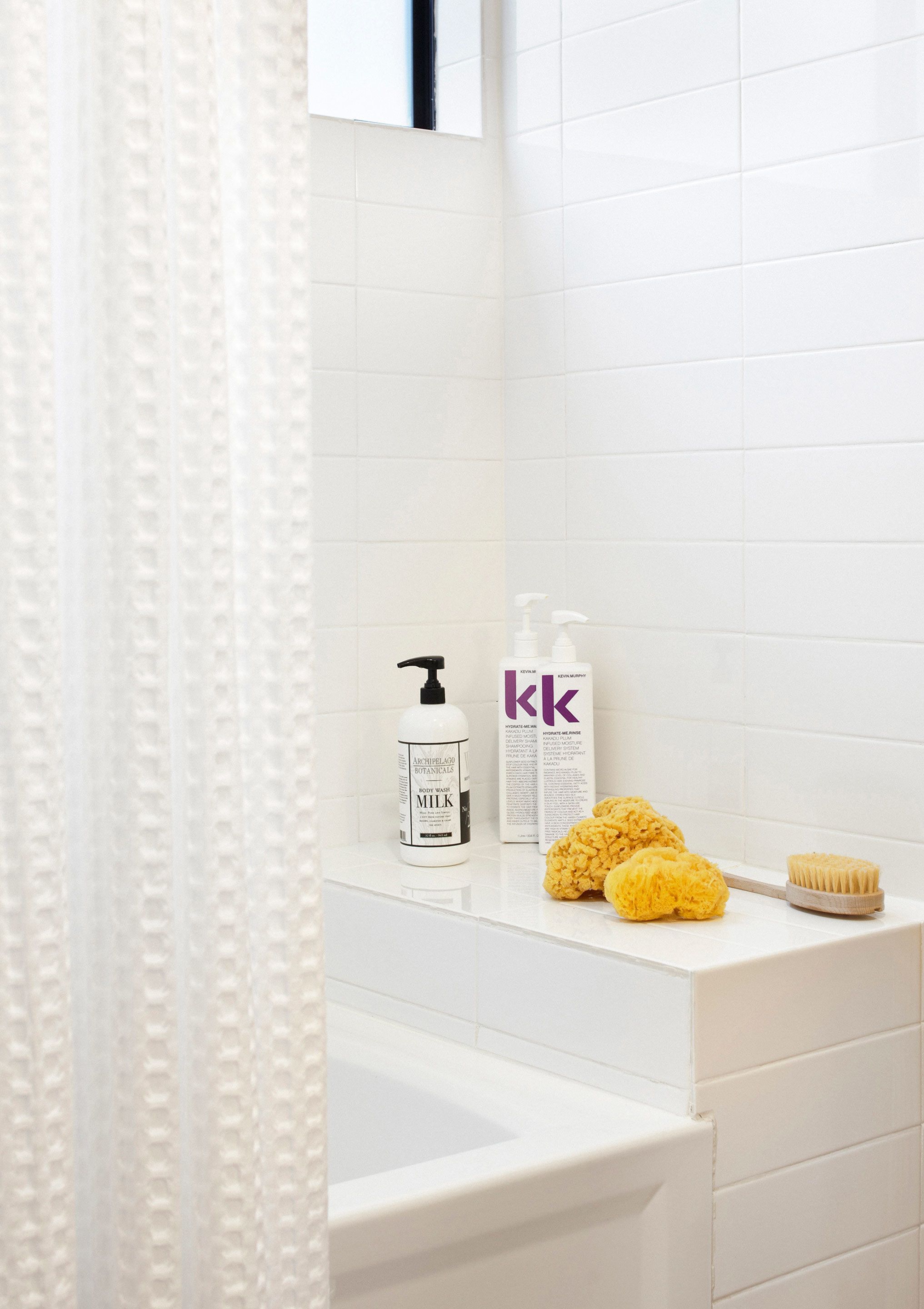 Une salle de bain avec une baignoire blanche, un rideau de douche et des articles de toilette posés sur le comptoir.