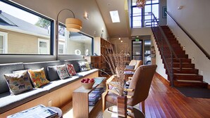 A modern interior with a wooden staircase, a built-in bench with cushions, and a view of the outside. - Heywood Hotel (Austin)