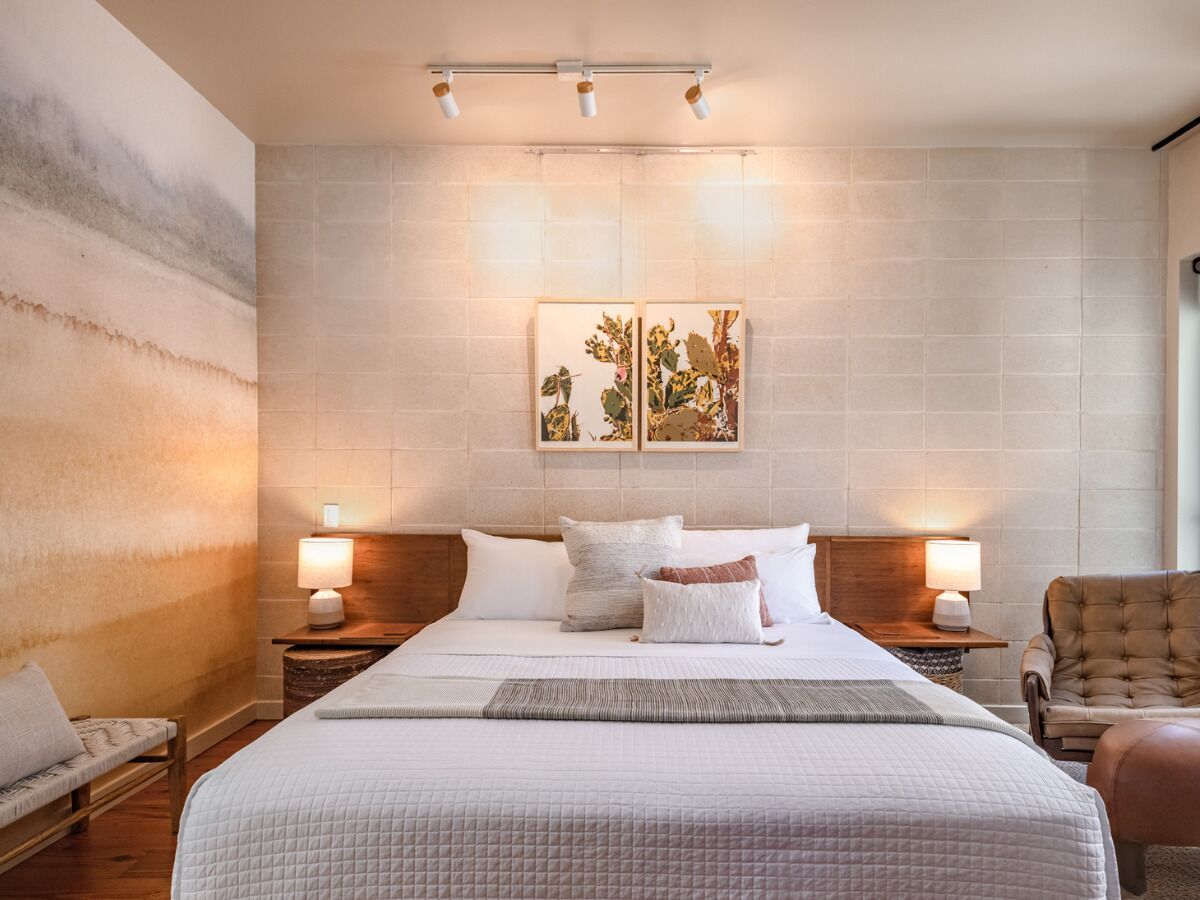 A bedroom with a large bed, two bedside tables with lamps, a chair, and a wall-mounted artwork.