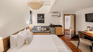 A modern bedroom with a large bed, a sofa, a desk, and a TV. - Heywood Hotel (Austin)