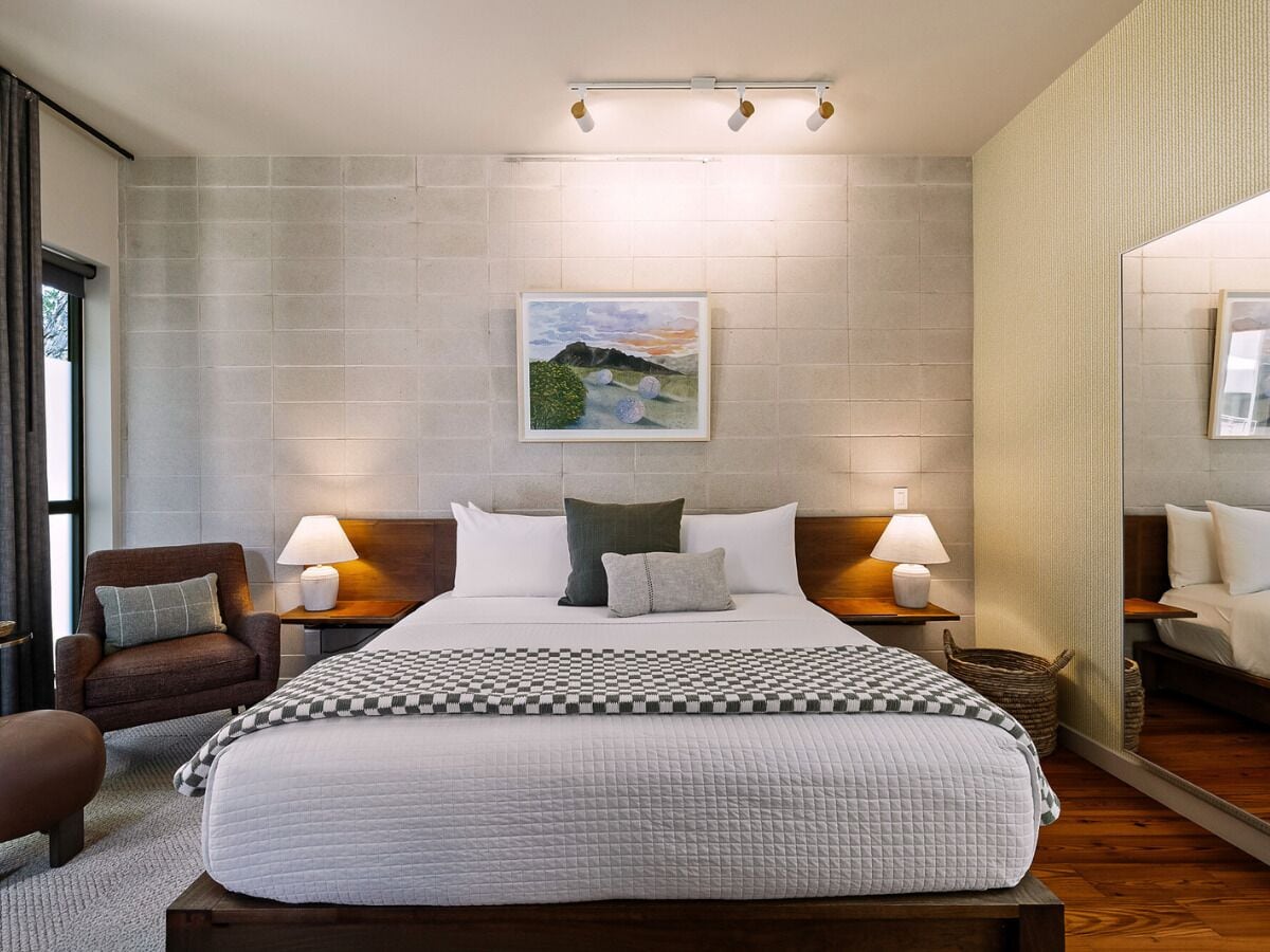 A modern hotel room with a large bed, two bedside tables with lamps, a chair, and a painting on the wall.