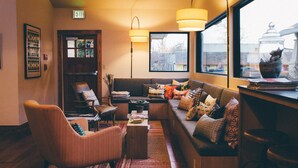A cozy living room with a sofa, armchairs, and a coffee table. There is a bookshelf, a window with a view, and a lamp. - Heywood Hotel (Austin)