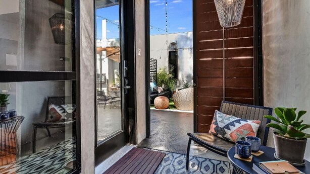 A modern outdoor seating area with a glass door leading to a patio, a wooden ceiling, and a hanging light fixture. - Heywood Hotel (Austin)