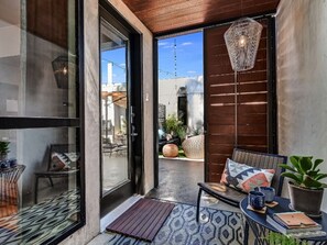 Un espacio moderno para sentarse al aire libre con puerta de cristal que da a un patio, techo de madera y una lámpara colgante.