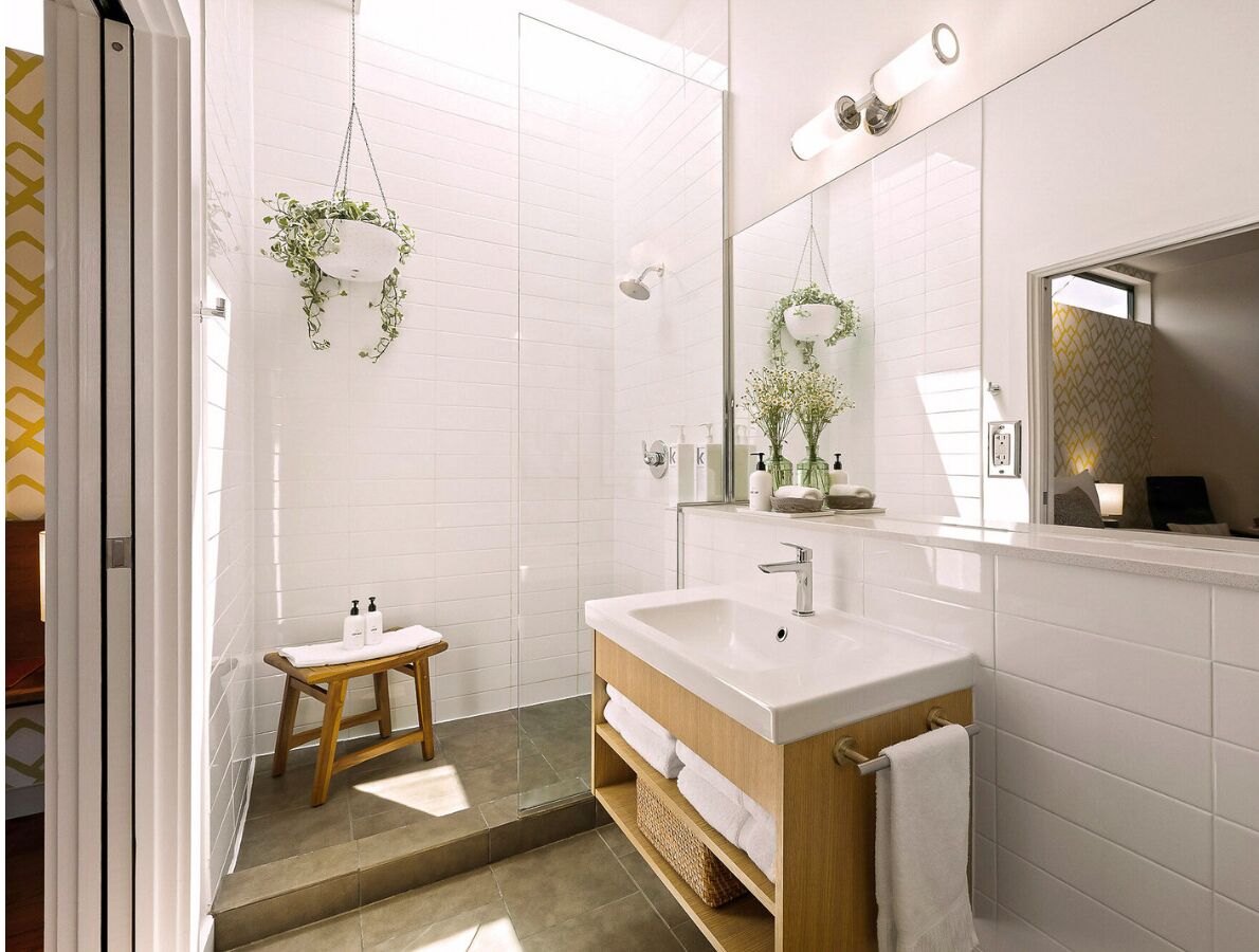A modern bathroom with a large mirror, a wooden vanity, a shower area, and hanging plants.