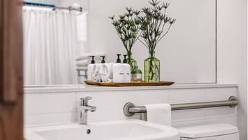 A bathroom with a sink, mirror, and toiletries on a shelf.