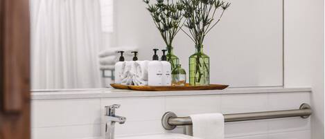A bathroom with a sink, mirror, and toiletries on a shelf.