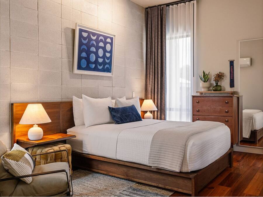 Ein modernes Hotelzimmer mit einem großen Bett, zwei Nachttischen mit Lampen, einem Schminktisch und einem Wandbild.