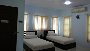 A room with two single beds, a door, an air conditioner, and a clock on the wall. - Bann Suan Rachawadee B&B (Sisaket)