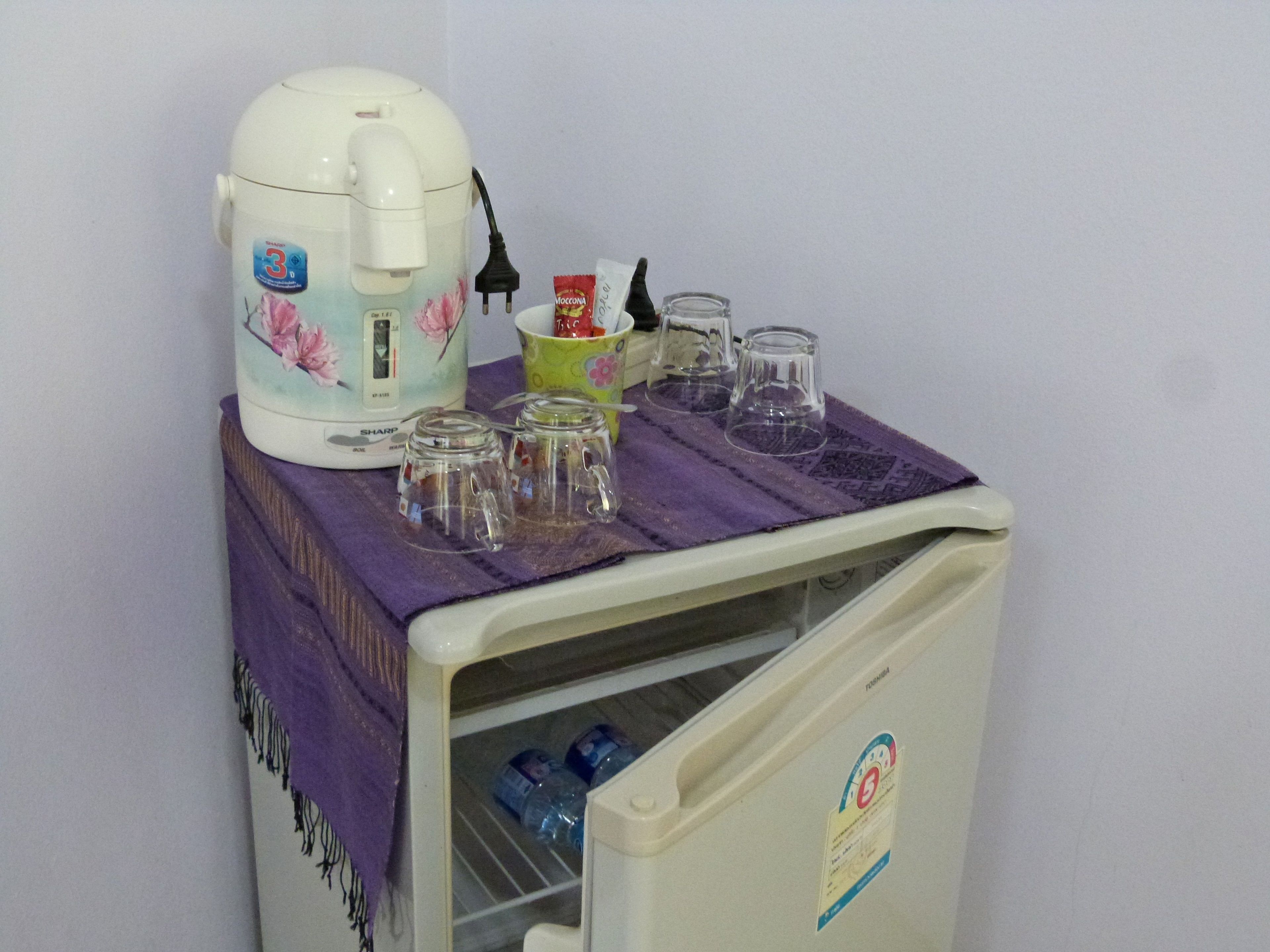 A small refrigerator with a coffee maker, two cups, and a mug on top.