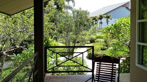 A covered outdoor seating area with a table and chairs, surrounded by greenery and a view of a building in the background. - Bann Suan Rachawadee B&B (Sisaket)
