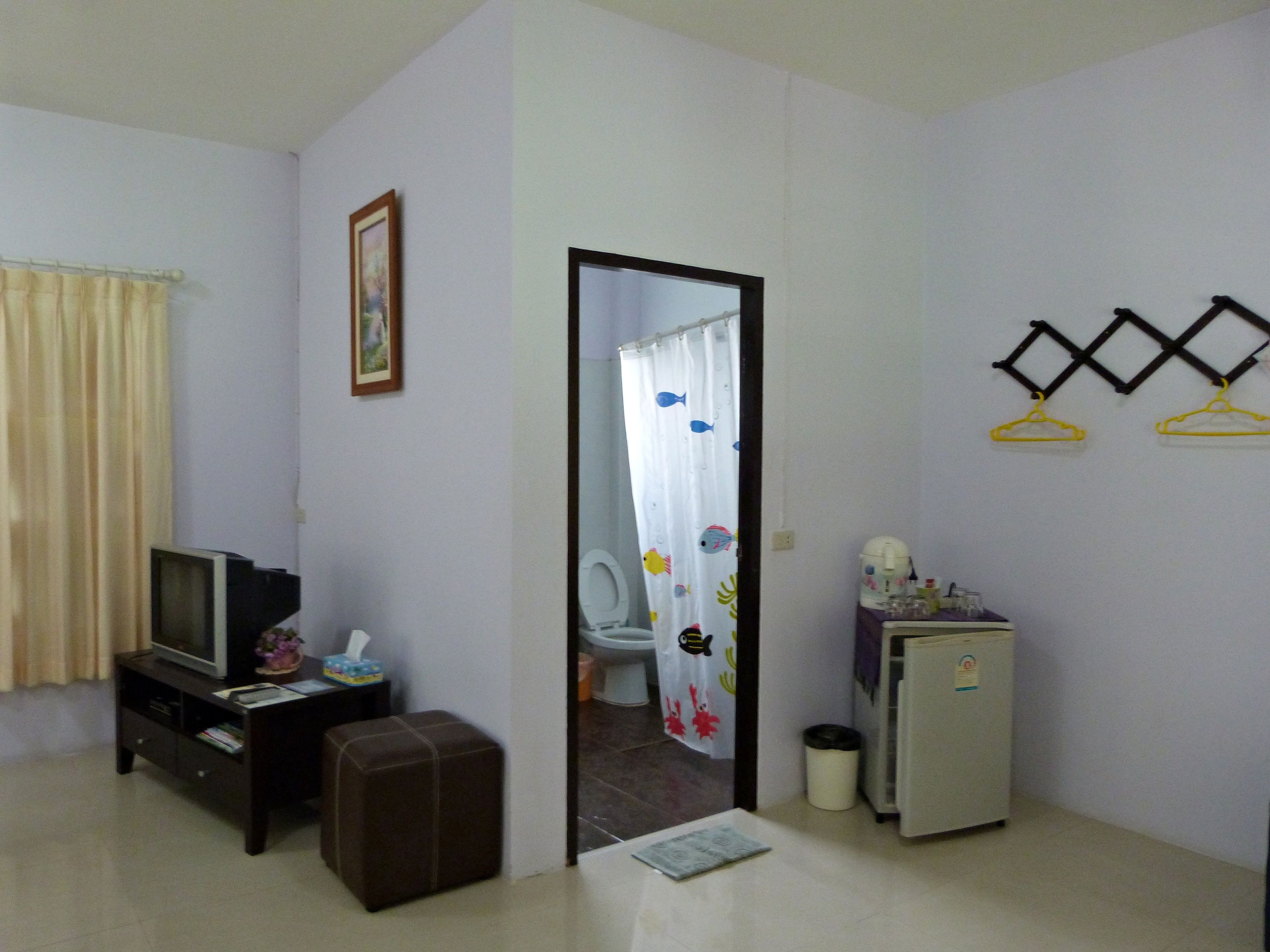 A small, sparsely furnished room with a television, a small refrigerator, a trash bin, and a door leading to a bathroom with a shower curtain.