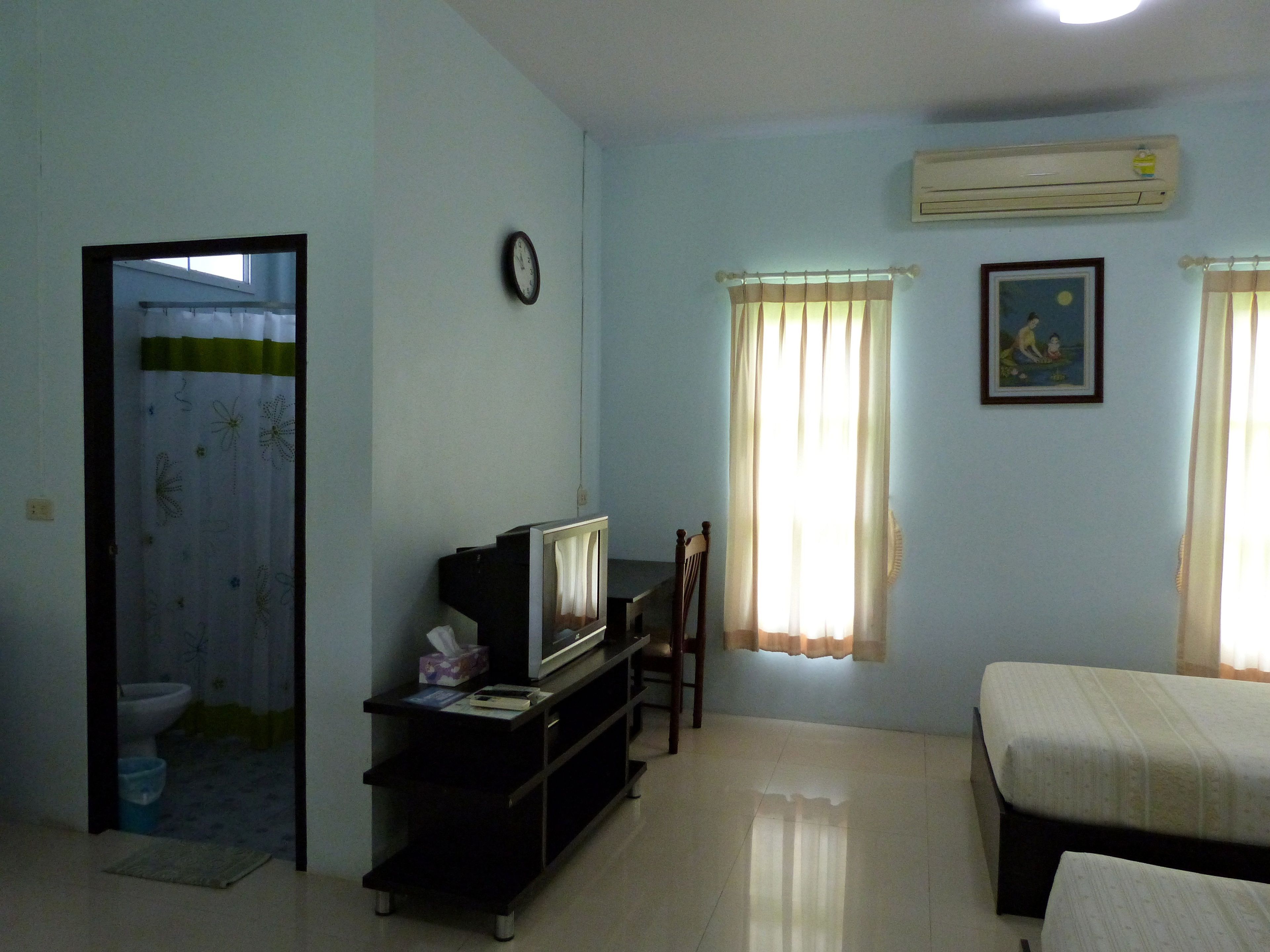 A room with a bed, a TV on a stand, a clock, and an air conditioner on the wall.